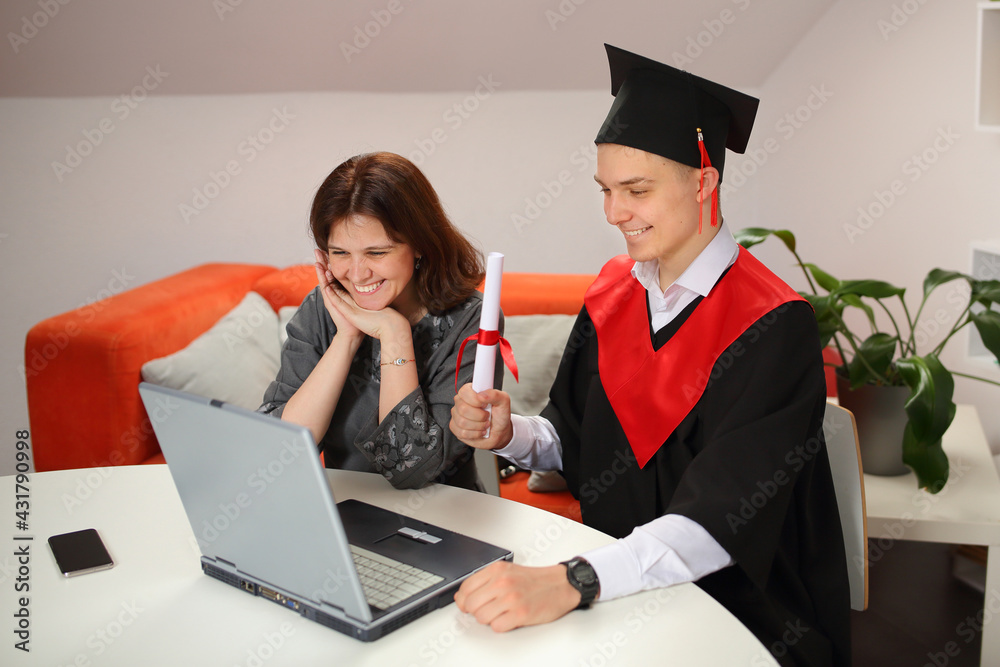 Mother looks at Laptop screen with happy students in graduation gown and a square cap during Virtual graduation ceremony - obrazy, fototapety, plakaty 