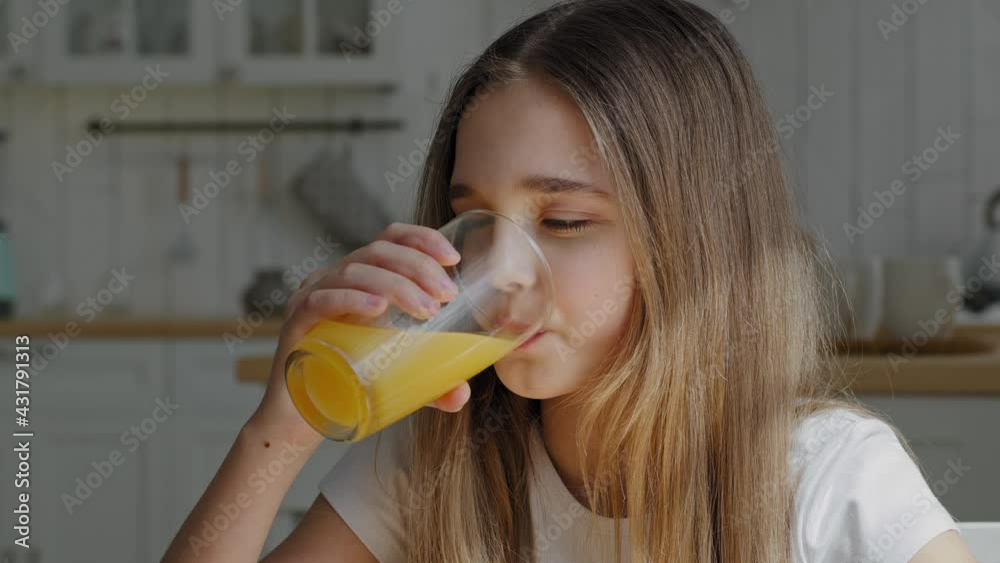 Portrait caucasian little school girl child daughter preteen kid feels thirsty drinks orange juice with tropical fruits vitamins enjoying refreshing taste sitting in kitchen smiling looking at camera Portrait caucasian little school girl child daughter preteen kid feels thirsty drinks orange juice with tropical fruits vitamins enjoying refreshing taste sitting in kitchen smiling looking at camera