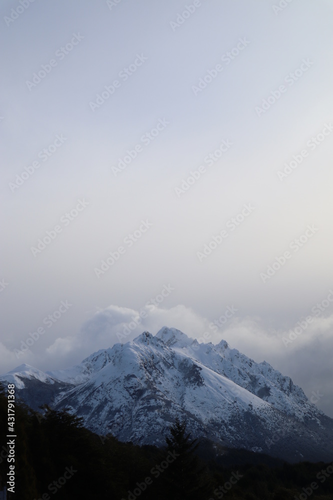 Astonishing shot of a peak from a snowy mountain in a windy cold day, the cloudy sky and the dark forest makes a perfect mystic scene in Patagonia 