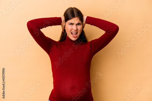Young caucasian pregnant woman isolated on beige background covering ears with hands trying not to hear too loud sound.