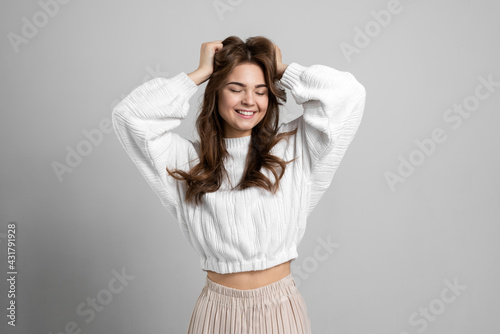 Charming young lady touches her dark hair on a gray background. Cute girl closed her eyes, posing beautifully against the background of an empty wall. © speed300