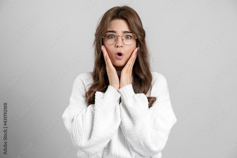 Surprised, shocked girl with glasses, touches her face with her hands. Emotional girl on a gray background Surprised, shocked girl with glasses, touches her face with her hands. Emotional girl on a gray background