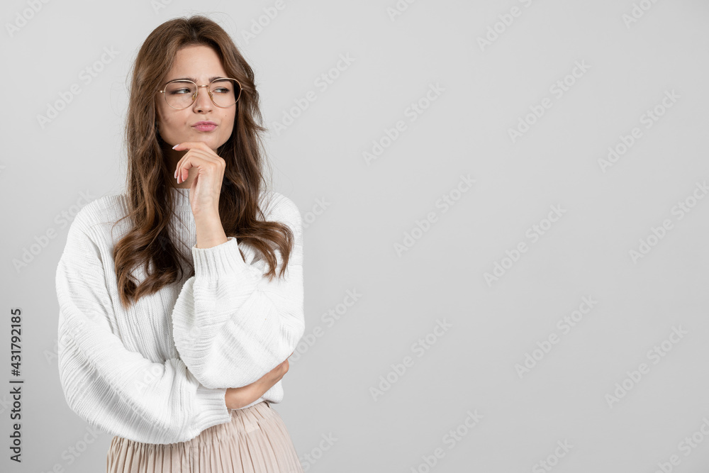 Conceived, serious girl touches her chin, looks away. Cute, focused brunette on a gray background Conceived, serious girl touches her chin, looks away. Cute, focused brunette on a gray background