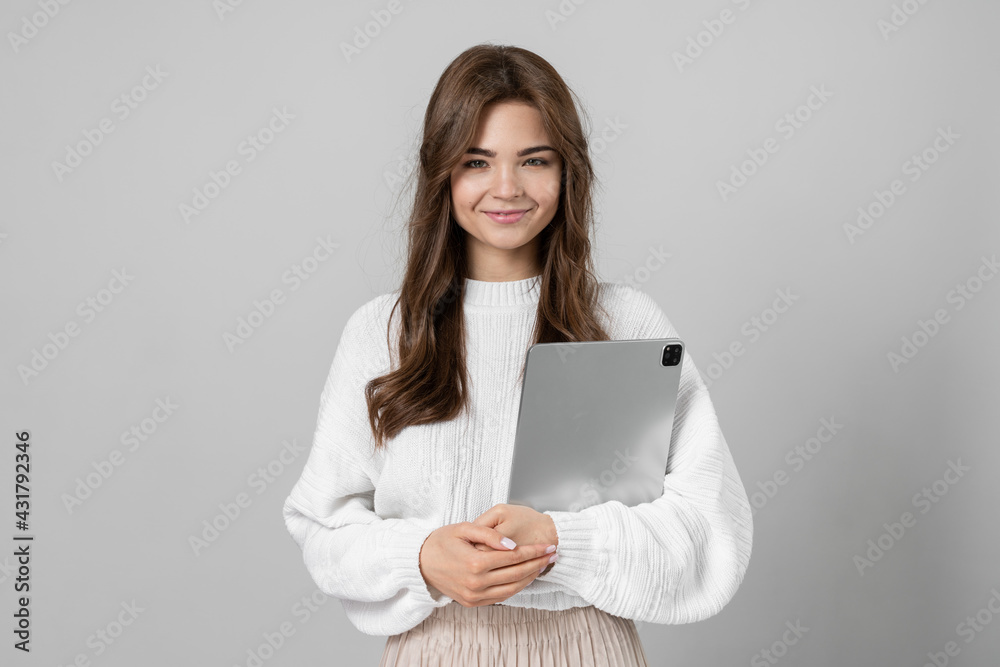 Attractive young lady holding a tablet in her hands. Beautiful girl isolated on a gray background Attractive young lady holding a tablet in her hands. Beautiful girl isolated on a gray background