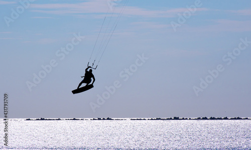 The silhouette of a kitesurfer hovers in the air over the sea. The water glistens in the sun.