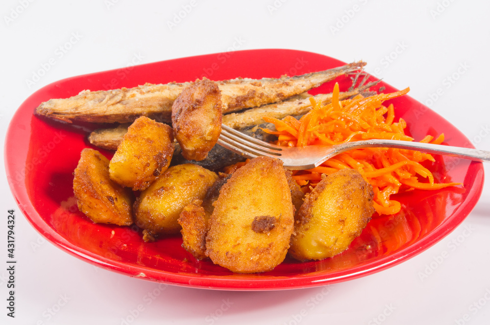 Homemade dish - fried potato wedges with small fish and pickled carrots on a red plate, simple rustic food, close-up. Homemade dish - fried potato wedges with small fish and pickled carrots on a red plate, simple rustic food, close-up.