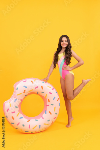 happy beach child in swimsuit with doughnut inflatable ring on yellow background, waterpark.