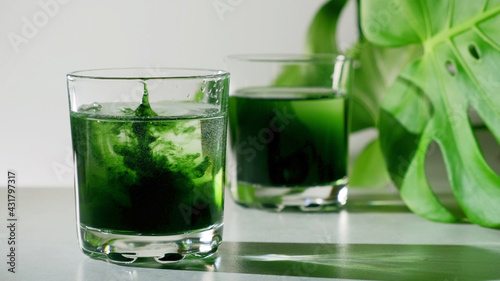 Chlorophyll extract is poured in pure water in glass against a white grey background with green leaf. Liquid chlorophyll in a glass of water. Concept of superfood, healthy eating, detox and diet photo