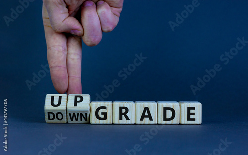 Upgrade or downgrade symbol. Businessman turns wooden cubes and changes words 'downgrade' to 'upgrade'. Beautiful grey table, grey background, copy space. Business and upgrade or downgrade concept.
