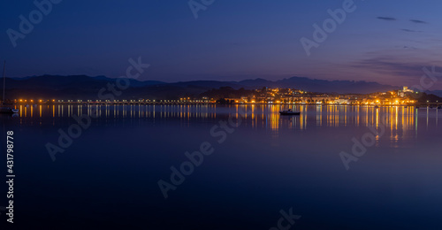 Panorámica nocturna del puente de San Vicente de la Barquera iluminado , con los reflejos de las luces de colores en el mar, y las barcas meciéndose en el agua, en Santander, España, verano de 2020.