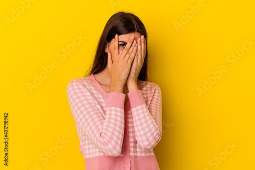 Young caucasian woman isolated on yellow background blink through fingers frightened and nervous.