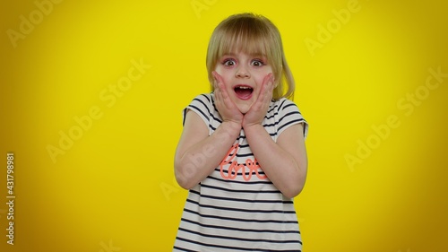 Oh my god, wow. Excited amazed blonde child girl 5-6 years old raising hands in surprise looking at camera with big eyes, shocked by sudden victory on yellow studio background. Teen kid children