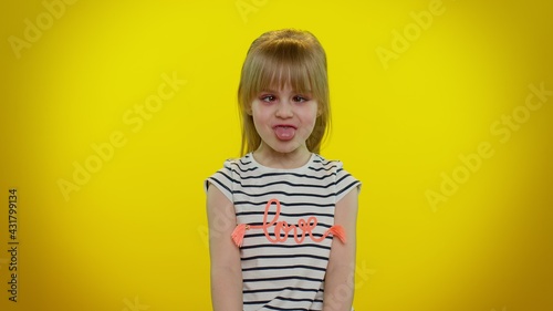 Cute funny teen child kid girl making playful silly facial expressions and grimacing, fooling around, showing tongue. Posing isolated on yellow studio background. Childhood lifestyle. Young children