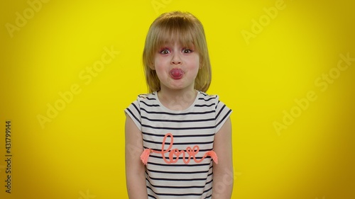 Cute funny teen child kid girl making playful silly facial expressions and grimacing, fooling around, showing tongue. Posing isolated on yellow studio background. Childhood lifestyle. Young children