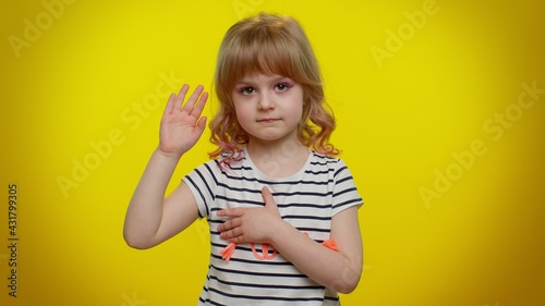 I swear to be honest. Responsible sincere little kid child in shirt raising hand to take oath, promising to be honest and to tell truth, keeping hand on chest on yellow wall. Children girl emotions