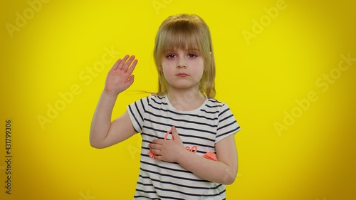 I swear to be honest. Sincere responsible cute kid child 5-6 years old raising hand to take oath, promising to be honest and to tell truth, keeping hand on chest on yellow wall. Children girl emotions