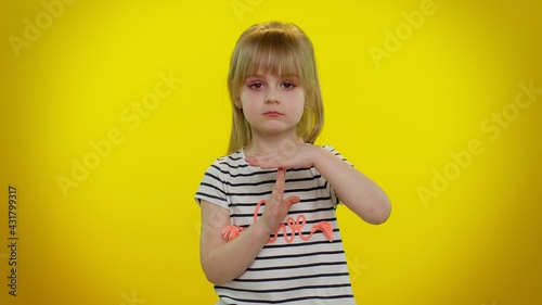 Tired serious upset blonde child girl 5-6 years old in striped t-shirt showing time out gesture, limit or stop sign, no pressure, i need more time on yellow studio wall background. Teen kid children