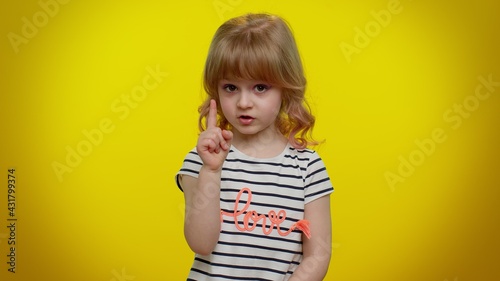 Hey you, be careful. Cute kid child girl 5-6 years old warning with admonishing finger gesture, saying no, scolding and giving advice to avoid danger, disapproval sign on yellow studio wall background
