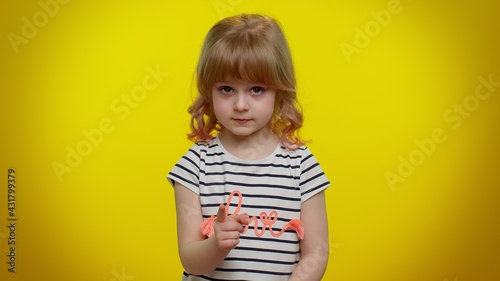 I am warning you. Cute kid child girl 5-6 years old warning with admonishing finger gesture, saying no, scolding and giving advice to avoid danger, disapproval sign on yellow studio wall background