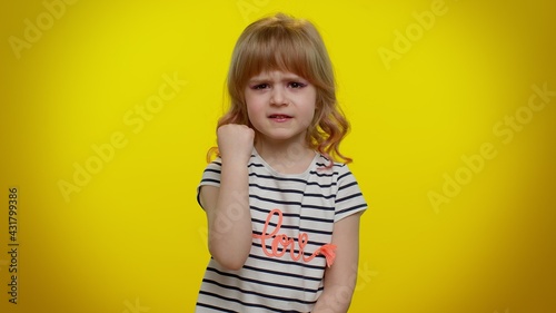 Funny aggressive cute blonde kid child 5-6 years old in t-shirt trying to fight at camera, shaking fist, boxing with expression, punishment on yellow studio background. Teenager children girl emotions