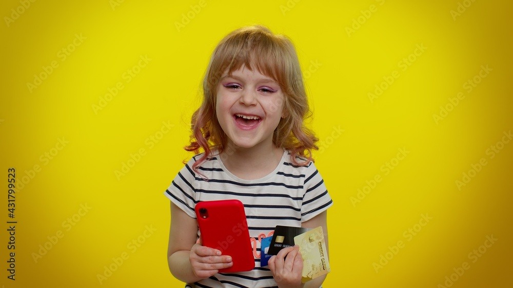 Happy excited joyful little blonde child kid girl use mobile cell phone and plastic credit bank card, browsing say wow yes, found out great big win, doing winner gesture, purchases online shopping Happy excited joyful little blonde child kid girl use mobile cell phone and plastic credit bank card, browsing say wow yes, found out great big win, doing winner gesture, purchases online shopping