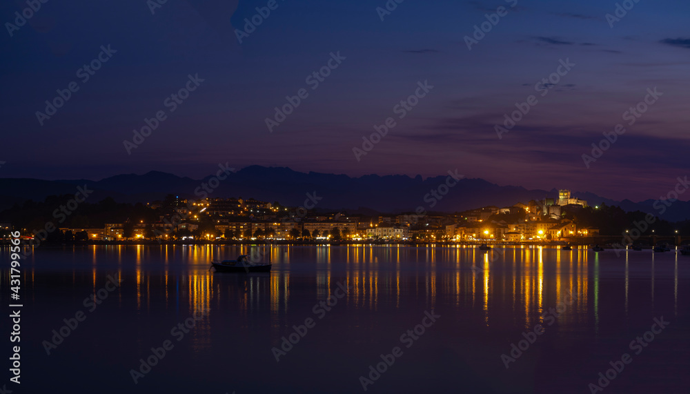 Panorámica nocturna del puente de San Vicente de la Barquera iluminado , con los reflejos de las luces de colores en el mar, y las barcas meciéndose en el agua, en Santander, España, verano de 2020.