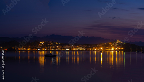 Panorámica nocturna del puente de San Vicente de la Barquera iluminado , con los reflejos de las luces de colores en el mar, y las barcas meciéndose en el agua, en Santander, España, verano de 2020. © acaballero67