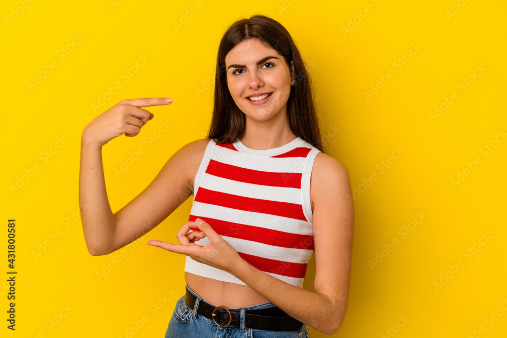Young caucasian woman isolated on yellow background holding something little with forefingers, smiling and confident. Young caucasian woman isolated on yellow background holding something little with forefingers, smiling and confident.