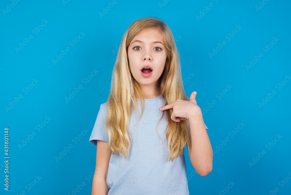 beautiful Caucasian little girl wearing white T-shirt over blue background being in stupor shocked, has astonished expression pointing at oneself with finger saying: Who me? beautiful Caucasian little girl wearing white T-shirt over blue background being in stupor shocked, has astonished expression pointing at oneself with finger saying: Who me?