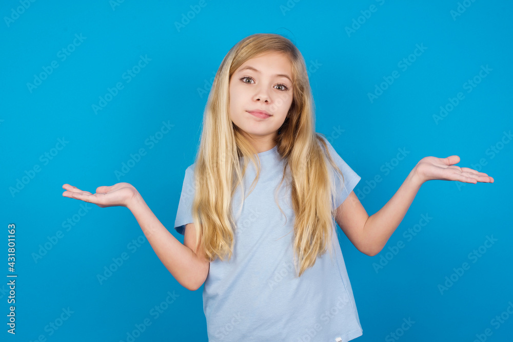 Maybe yes or no. Doubtful beautiful Caucasian little girl wearing white T-shirt over blue shrugs shoulders in bewilderment, tries to make decision puzzled what he wants. Hesitation and uncertainty. Maybe yes or no. Doubtful beautiful Caucasian little girl wearing white T-shirt over blue shrugs shoulders in bewilderment, tries to make decision puzzled what he wants. Hesitation and uncertainty.