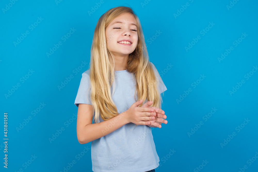 beautiful Caucasian little girl wearing blue T-shirt over blue background, feeling happy, smiling and clapping hands, saying congratulations with an applause.