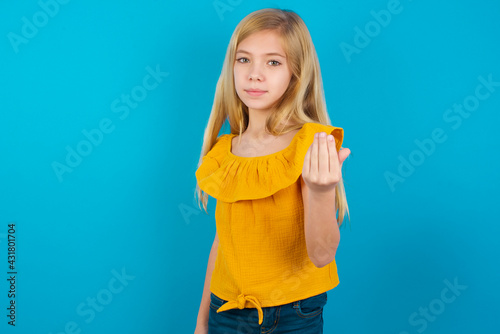 Caucasian kid girl wearing yellow T-shirt against blue wall inviting to come with hand. Happy that you came