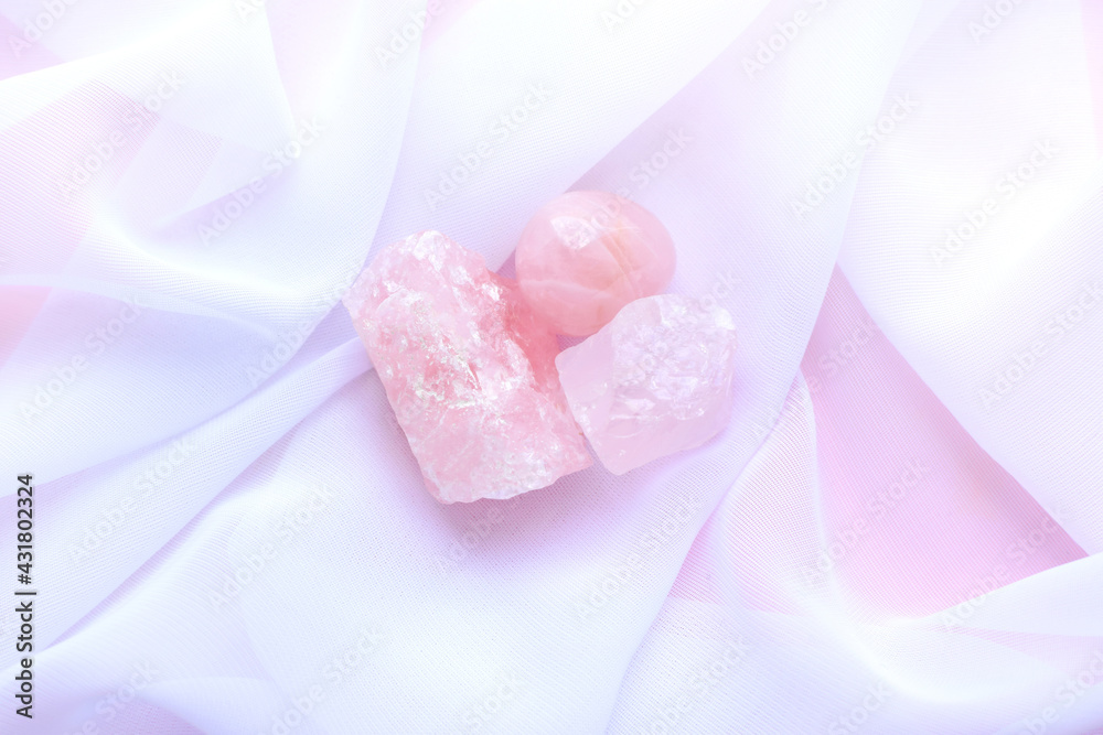 Minerals of gemstones on a pink background. Rough stones and tumbled rose quartz on a white transparent fabric.