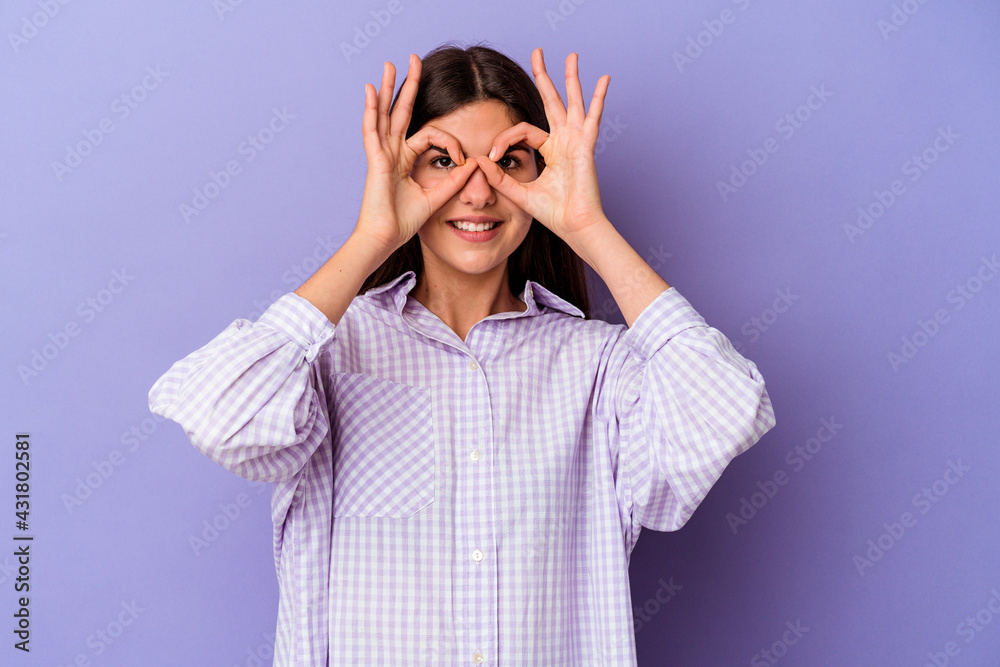 Young caucasian woman isolated on purple background showing okay sign over eyes Young caucasian woman isolated on purple background showing okay sign over eyes