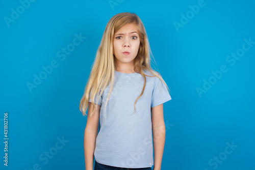 beautiful Caucasian little girl wearing blue T-shirt over blue background expressing disgust, unwillingness, disregard having tensive look frowning face, looking indignant with something. © Jihan