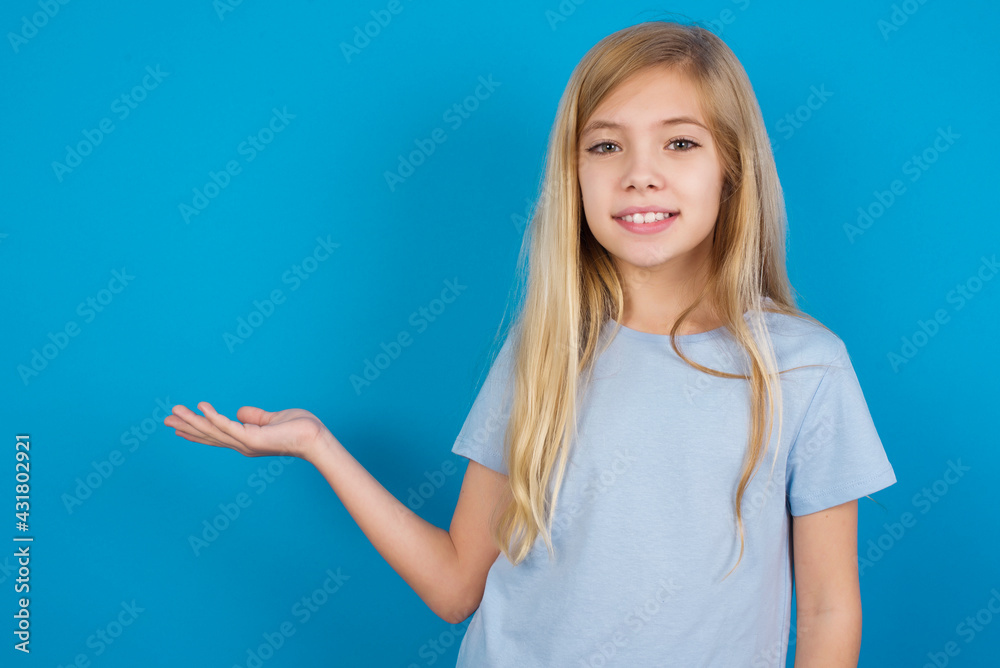 Positive glad beautiful Caucasian little girl wearing blue T-shirt over blue says: wow how exciting it is, has amazed expression, shows something on blank space with open hand. Advertisement concept. Positive glad beautiful Caucasian little girl wearing blue T-shirt over blue says: wow how exciting it is, has amazed expression, shows something on blank space with open hand. Advertisement concept.
