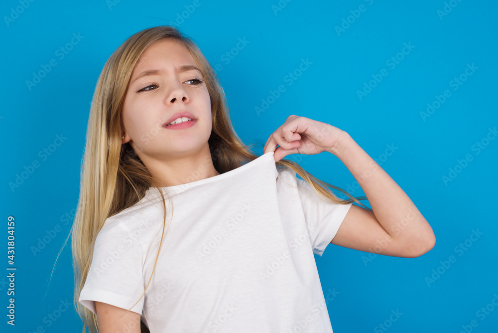 Fototapeta premium beautiful Caucasian little girl wearing white T-shirt over blue background stressed, anxious, tired and frustrated, pulling shirt neck, looking frustrated with problem