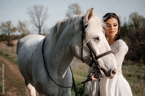 A beautiful bride in a light dress poses. Boho style. Photo shoot with a horse.