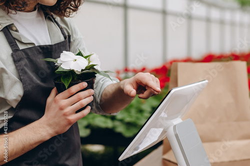 Fotografie Male attractive florist selling flowerpot in the garden centre, standing near tablet