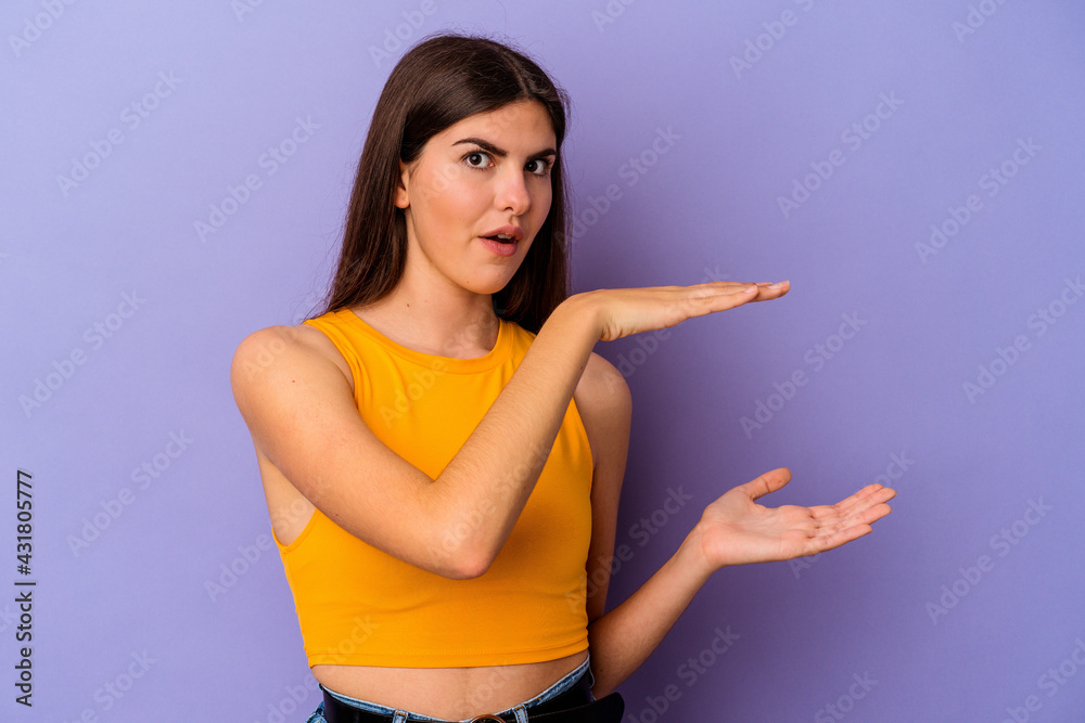 Young caucasian woman isolated on purple background holding something with both hands, product presentation. Young caucasian woman isolated on purple background holding something with both hands, product presentation.