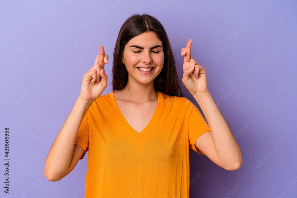 Young caucasian woman isolated on purple background crossing fingers for having luck Young caucasian woman isolated on purple background crossing fingers for having luck