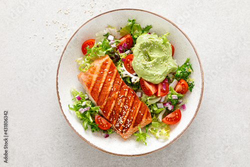 Grilled salmon fish fillet and fresh green lettuce vegetable tomato salad with avocado guacamole. Top view