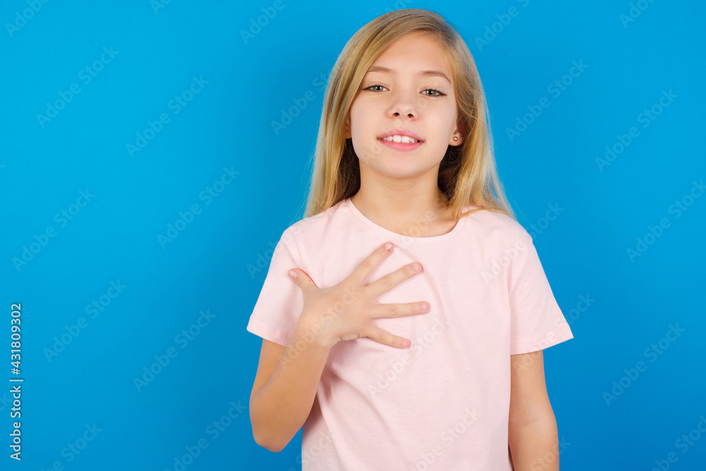 Caucasian kid girl wearing pink shirt against blue wall smiles toothily cannot believe eyes expresses good emotions and surprisement Caucasian kid girl wearing pink shirt against blue wall smiles toothily cannot believe eyes expresses good emotions and surprisement