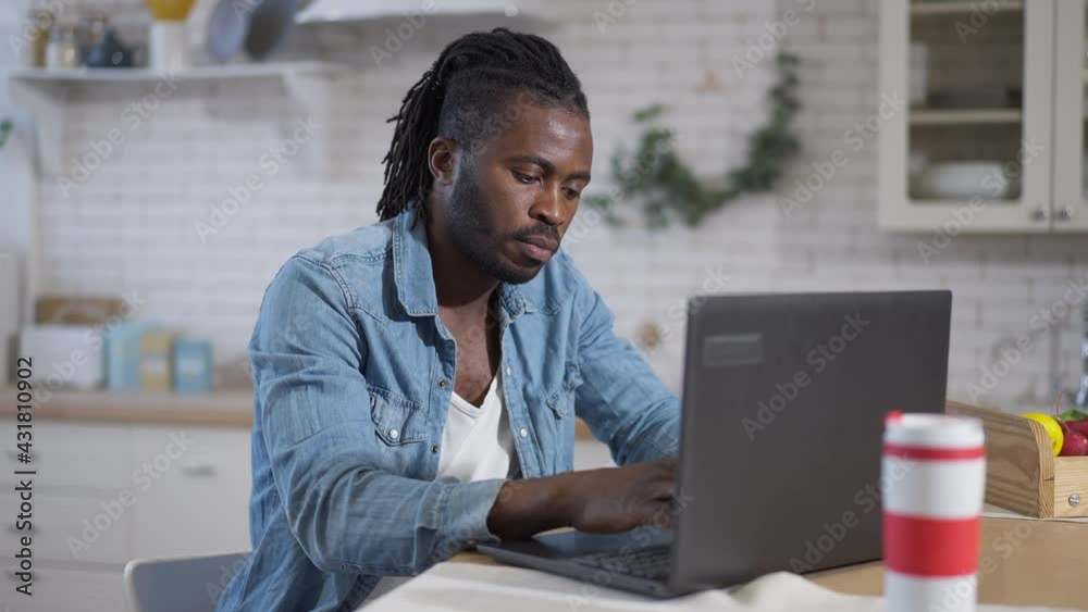 Concentrated African American male freelancer typing on laptop keyboard sitting in kitchen at home. Portrait of confident young handsome man messaging online from home office on Covid-19 lockdown Concentrated African American male freelancer typing on laptop keyboard sitting in kitchen at home. Portrait of confident young handsome man messaging online from home office on Covid-19 lockdown