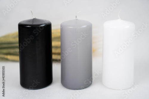 stylish black, gray and white candles on a white background with a sprig of dried flowers