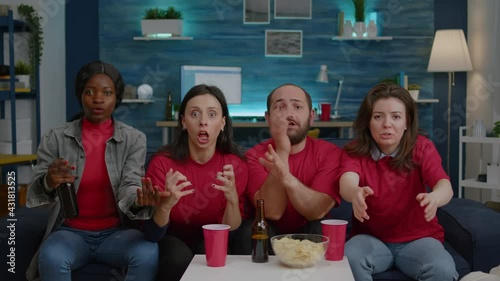 Happy multi-ethnic friends cheering together after foottball team winning sport championship. Support team watching soccer on television late at night while sitting on couch in living room photo