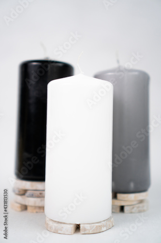 stylish candles black, gray and white stand on pieces of wood on a white background