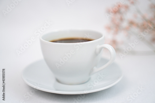 a cup of black coffee on a white table and with a sprig of dried flowers