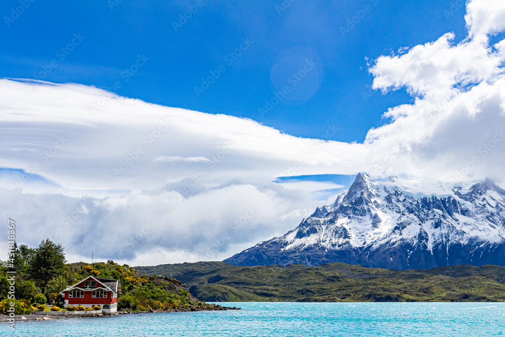Belo lago verde rodeado por montanhas e ao fundo cordilheira das Torres del Paine com muita neve, céu azul com nuvens.