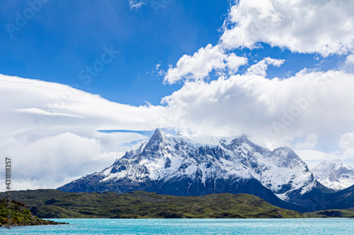 Belo lago de aguas verdes rodeado por montanhas e a cordilheira dos Andes ao fundo com muita neve, céu azul com nuvens.